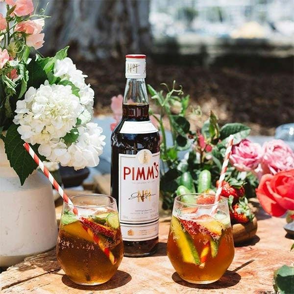 Two glasses of Pimm's cocktail with a Pimm's bottle in between them.