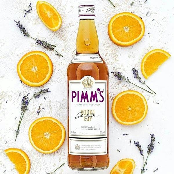 Bottle of Pimm's No. 7 Cup laid on a white surface surrounded by orange slices and lavender sprigs