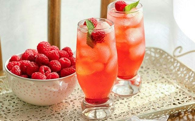 Two pink drinks in a highball glass with ice, mint and raspberries