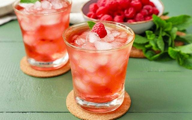 Two pink drinks in a rocks glass with ice, mint and raspberries