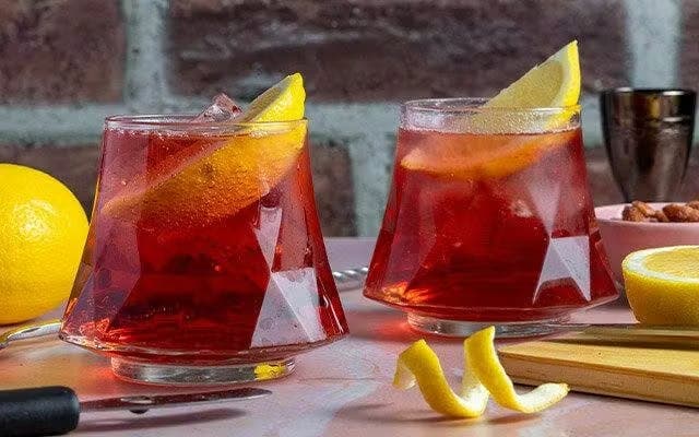 Two red cocktails in rocks glasses with lemon wedge garnishes