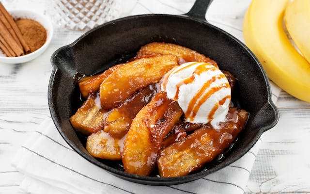 Cooked banana slices topped with a treacle sauce and vanilla ice cream in a black skillet