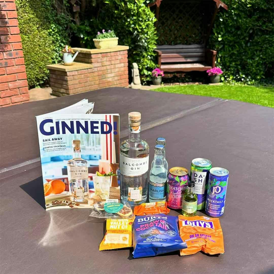 Craft Gin Club's May 2024 Gin of the Month items laid out on a table in a summer garden